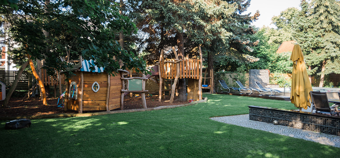 Rund um den bestehenden Pool sollte ein Spieleparadies für die Kinder und Entspannungsbereich für die Eltern entstehen. Ein Ort, an dem die Familie zusammenfindet und gemeinsam Zeit verbringen kann. Der Garten sollte individuell, detailverliebt, blütenreich sein und frisches Obst hervorbringen, damit die kleinen Naschkatzen eigens angebaute Leckereien pflücken können. Bereits im Herbst 2015 begannen die Gespräche und die Planungen, sodass nach dem Winter im März / April 2016 die Arbeiten begannen. Zu Beginn wurden Wurzeln entfernt und Leitungen und Kabel verlegt. Wege wurden geschaffen und gepflastert, Sitzplätze gestaltet und die Voraussetzungen für das Spiel- und Entdeckungsparadies hergestellt. Die Bauherren finden folgende Worte für unsere Arbeit und Leidenschaft: „Selbst zum Teil anhaltender Regen hielt Ihre Mitarbeiter nicht davon ab, den geplanten Fertigstellungstermin einzuhalten. Es war immer wieder eine Freude von der Arbeit nach Hause zu kommen und das neu Entstandene zu beobachten. Pünktlich zum Frühjahrsbeginn konnten dann die Arbeiten abgeschlossen werden und wir konnten unsere erste Familienfeier im neu gestalteten Garten durchführen. Alle waren begeistert. Nun sind die ersten Monate vergangen. Überall blüht es in den unterschiedlichsten Farben. Das erste Obst und Gemüse konnte geerntet werden und wir haben bereits viele Stunden der Erholung auf unserem Grundstück genießen können. Die Kinder nutzen den Rundweg als Rallye-Strecke mit ihren Tretautos und stellen Rundenrekorde auf. Wir möchten uns an dieser Stelle noch einmal ganz herzlich für Ihr Engagement und die tolle Arbeit bedanken. Aus heutiger Sicht würden wir jeder Zeit wieder ein derartiges Projekt mit Ihnen realisieren.“ Wir wünschen den Bauherren immer glücklich tobende Kinder und Zeit, das Familienleben zu genießen!